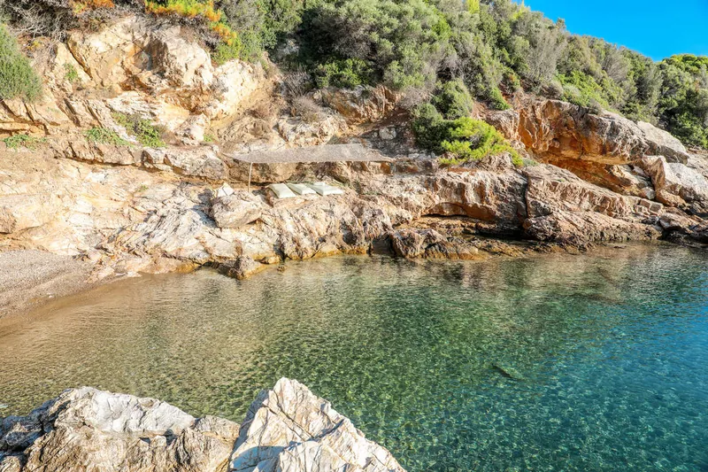 The cove of the private beach in clear green water, between golden rocks