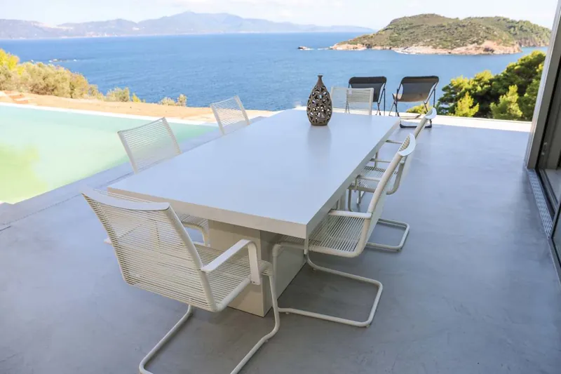 The long outdoor dining table by the pool, the sea beyond