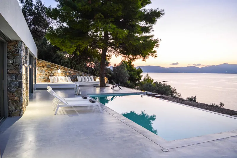 The infinity pool and the terrace under a pine at dusk, the sea and the mountains beyond